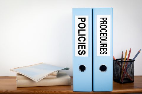 Policies and Procedures binders in the office. Stationery on a wooden shelf